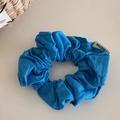 Detail of bright blue fabric scrunchie with textured cotton material and brand tag - Blue