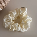 Close-up of cream fabric scrunchie with brand label on natural beige background - White