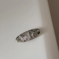 Detailed macro view of an oval acetate hair clip featuring grey marble texture and France logo - Off-White