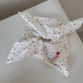Detail of white fabric hair tie featuring multi-colored polka dots and a brand tag - Multicolor Polka Dot Bow Tie Scrunchie