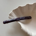 Macro view of slender acetate hair clip featuring purple marbled pattern and gold logo detail - Blue Purple