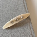 Detailed view of floral rhinestone pattern on cream oval hair clip with spring closure - Off White