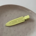 Makro-Detail einer neongelben matten Entenschnabel-Haarklammer auf einer Keramikschale - Grün