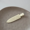 Detailansicht der matt cremegelben Haarspange aus Metall auf einem Keramikteller - Weiß
