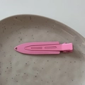 Detailed top view of a long pink metal duckbill hair clip on a ceramic tray - Rose Red