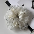 Close-up of white translucent tulle scrunchie with black polka dots on a magazine - White
