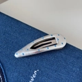 Gros plan d'une pince à cheveux en cuir argenté à pois bleu clair sur un fond denim - Pince Pois Bleus Cuir Argenté - Goutte d'Eau