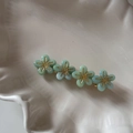 Gros plan de quatre pinces à cheveux fleurs vert menthe avec centres dorés sur plat - Vert