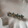 Gros plan de quatre fleurs en résine bleu et blanc sur pince dorée sur plateau blanc - Blanc Vert