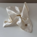 Detailaufnahme des cremefarbenen Satin-Haargummis mit Kamelientextur und goldener Metallschnalle - Weiße Rose Jacquard
