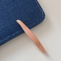 Macro shot of slender pink willow leaf hair clip on denim with gold handmade lettering - Orange Pink Pearl