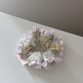 Vue macro d'un chouchou floral vert clair avec bords à volants en satin rose et petite étiquette - Frais à Volants Petit-Rose