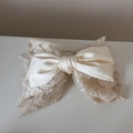 Close-up of cream satin ribbon and elegant lace texture on the large bow hair claw clip - Off White