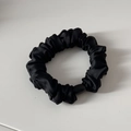 Detail eines schwarzen Satin-Scrunchies mit Falten und poliertem Harz-Verbindungsteil - Schwarz