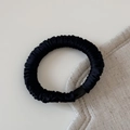 Detail of a black silk scrunchie with fine pleats and a sleek resin bead ornament - Black