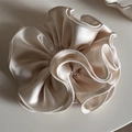 Detalle macro de scrunchie de satén crema con borde de volantes y textura perlada - Blanco Roto