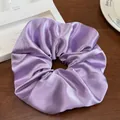 Vue détaillée du chouchou géant en satin violet avec texture soyeuse sur bois sombre - Lilas