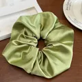 Gros plan sur le chouchou géant en satin vert avocat avec texture soyeuse sur bois chic - Vert Cardamome