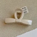 Macro shot of cream-white bow hair claw clip with golden metal spring on knit texture - Beige Bow Style