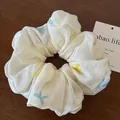 Elegant cream silk scrunchie with colorful embroidered bow patterns on wooden surface - Off White