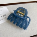 Detail view of a large blue shark hair claw clip with golden metal spring on grey surface - Elegant Blue