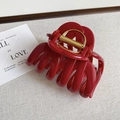 Detailed view of the large deep red hair claw clip with golden spring on beige fabric - Fashion Red