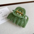 Detail view of a matte green shark hair claw clip with golden metal spring on fabric - Fresh Green