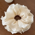 Close-up of cream pleated mesh scrunchie with layered ruffle texture on wooden table - Beige