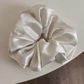 Detail of glossy cream satin scrunchie showing the smooth silk-like fabric texture - White