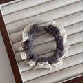 Detailed close-up of dark grey lace scrunchie with white trim and grey bead on velvet tray - Gray
