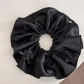 Detailed macro view of large black satin scrunchie with bows and silver brand tag - Black