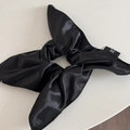 Detail of black glossy satin scrunchie with long bow and white text brand logo tag - Black