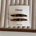 Detail of two tortoise shell acetate hair clips with gold logo on a beige jewelry tray - Dark Tortoiseshell