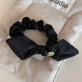 Close-up of black satin bow hair tie with a round gold charm on a textured background - Black