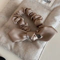 Detailed macro view of champagne gold satin bow hair tie with engraved metal plate - Apricot