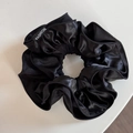 Détail d'un chouchou plissé noir en satin avec éclat métallique et étiquette logo - Chouchou noir