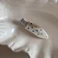 Dettaglio del fermaglio bianco con strass colorati su un piatto di ceramica - Albicocca Beige