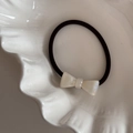 Détail d'un chouchou à nœud en acétate crème avec élastique noir sur un plateau blanc - Style Nacré / Blanc