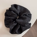 Detail eines schwarzen Satin-Haargummis mit silbernen Pailletten und Schleifenetikett - Schwarz