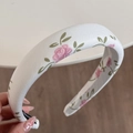 Nahaufnahme eines dicken Blumen-Stirnbandes mit rosa Rosen auf weißem Satin-Stoff - Haarreif im chinesischen Stil - Kleine Rose