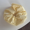 Detalle de un scrunchie plisado amarillo crema con etiqueta Hand Made sobre fondo blanco - Coletero / Amarillo