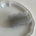 Detail einer grauen Haarklammer mit Wellenkante und Perlmuttglanz auf weißem Tablett - Grau