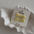 Close-up of two mini cream yellow bow hair clips displayed on a white shell plate - One Pair / Yellow