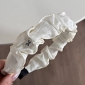 Dettaglio del cerchietto bianco in tessuto plissettato con logo a fiocco e punte antiscivolo - Cerchietto in Garza Plissettata Bianca