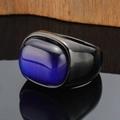 Macro shot of wide black metal ring with a purple cat-eye stone on wood background - Black Base Blue Gemstone