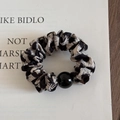 Dettaglio dello scrunchie leopardato con una perla nera lucida su cartoncino - Beige