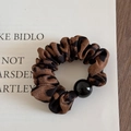 Dettaglio di elastico per capelli leopardato con perla nera su sfondo bianco pulito - Caffè scuro