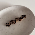 Detail einer wellenförmigen Haarklammer mit Leopardenmuster auf weißem Keramiktablett - Wellen-Haarnadel