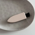 Minimalist beige leather hair clip with black metal base on a grey ceramic tray - Beige