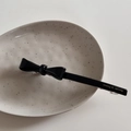 Détail d'une barrette noeud en acétate noir avec lettrage doré posée sur une assiette en céramique - Noir
